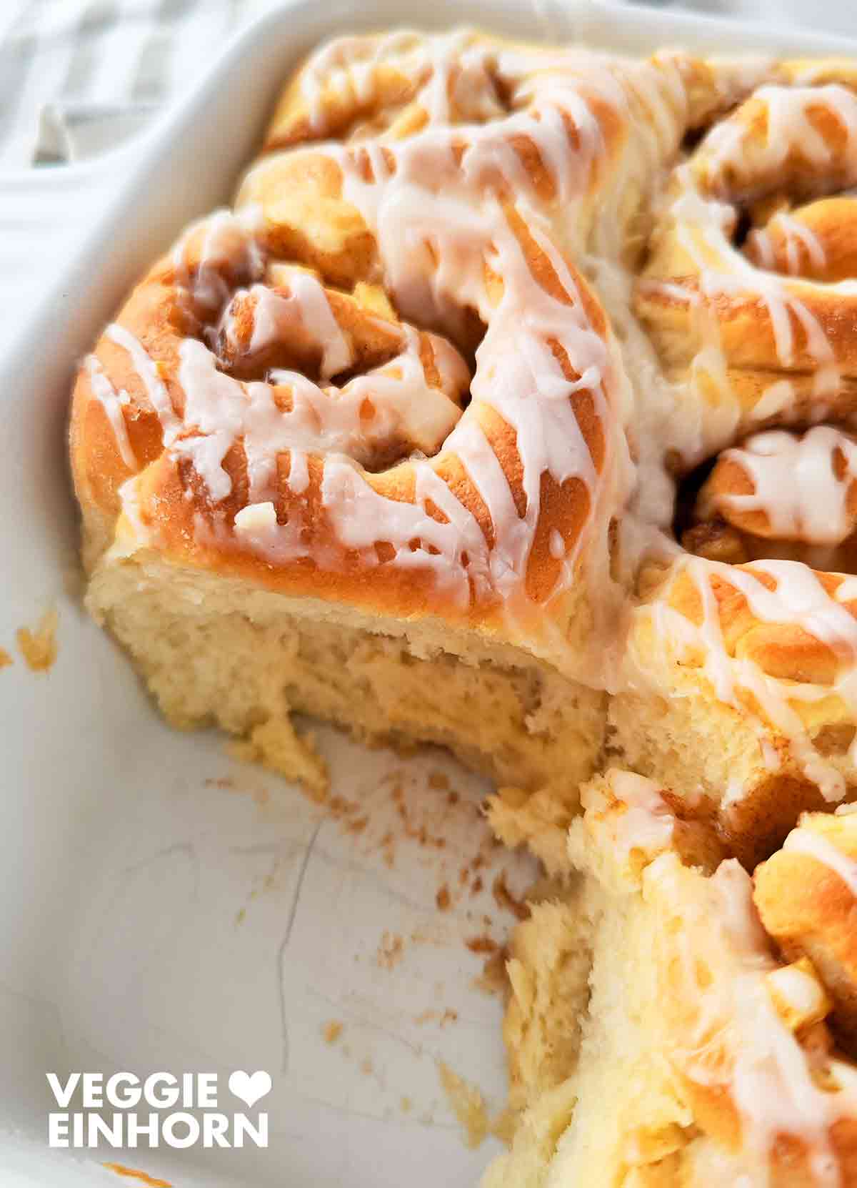 Nahaufnahme einer weißen Backform mit Apfel-Zimt-Schnecken, eine Schnecke fehlt bereits.
