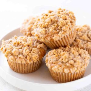 Vegane Apfel-Zimt-Muffins mit Streuseln auf einem weißen Teller.