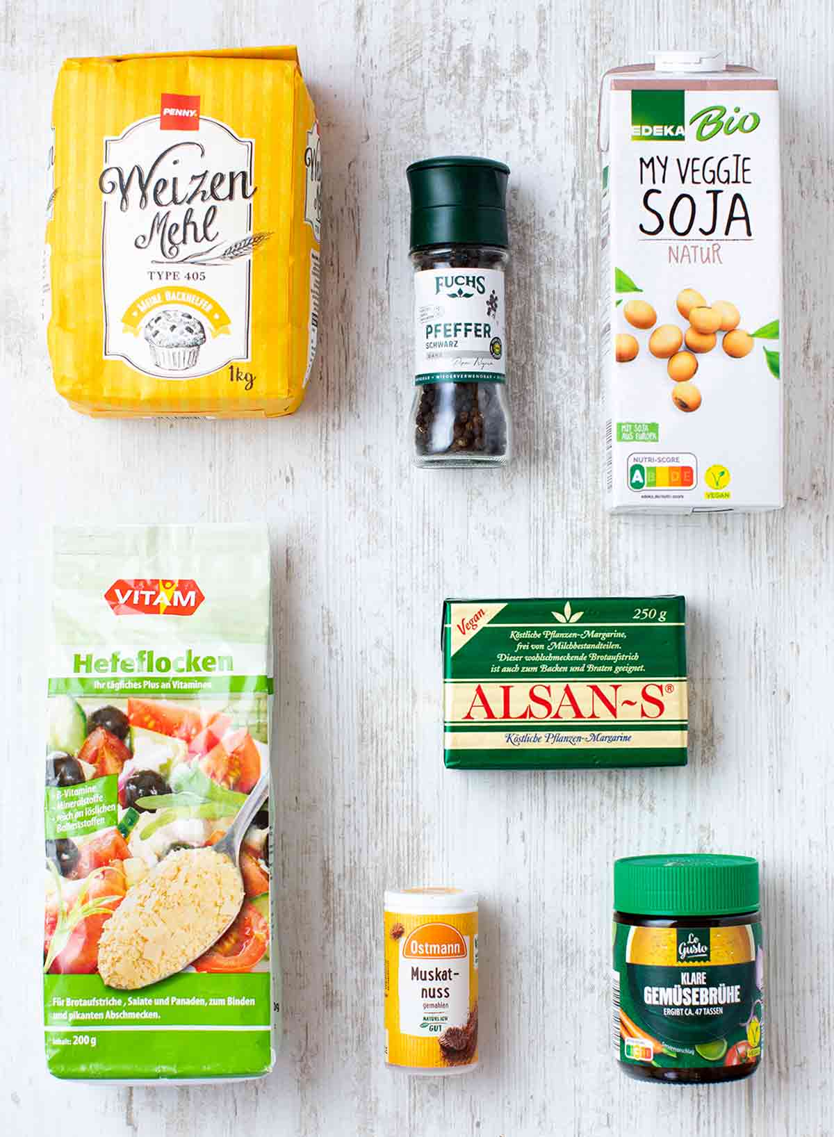 Verpackte Produkte für vegane Béchamelsauce: Weizenmehl, Pfeffer, Sojamilch, Hefeflocken, Muskatnuss, Alsan-Margarine und Gemüsebrühe Pulver.