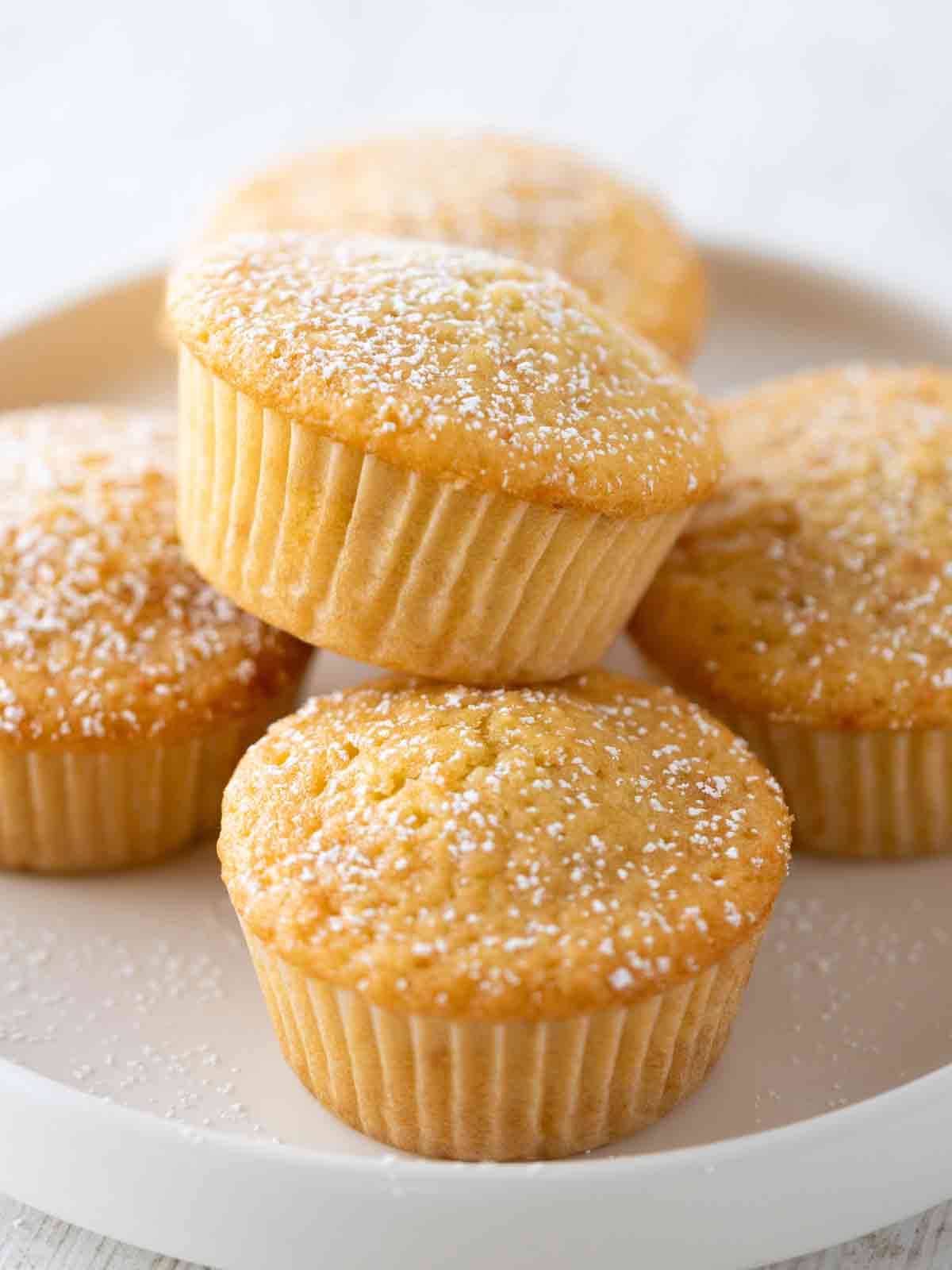 Nahaufnahme von veganen Muffins in Papierförmchen, mit Puderzucker bestäubt, auf einem weißen Teller.