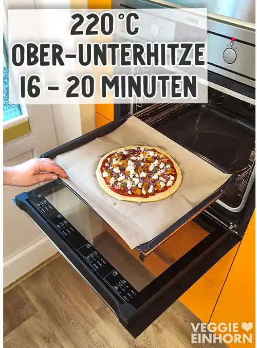 Mit veganem Gyros und veganem Feta belegte Pizza wird auf einem Backblech in den vorgeheizten Ofen geschoben.