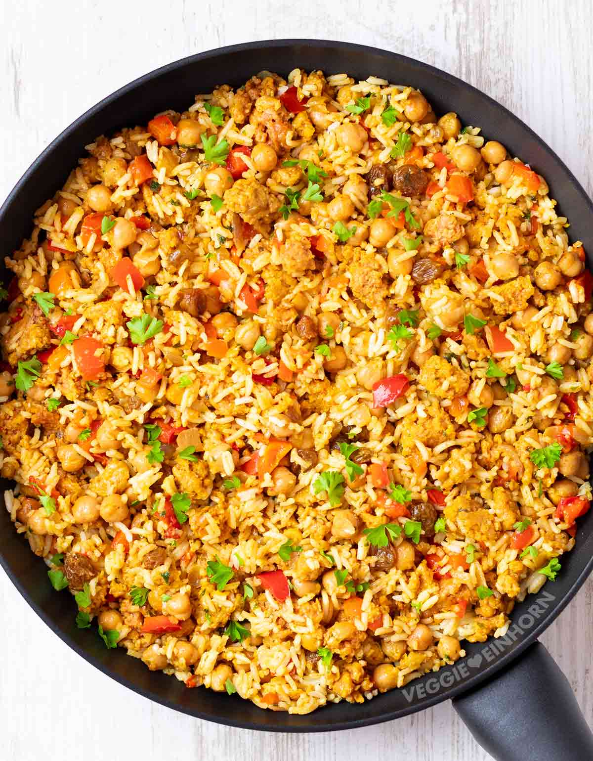 Pfanne mit bunter veganer Hackfleisch-Reis-Pfanne mit Kichererbsen, Paprika und frischer Petersilie von oben fotografiert.
