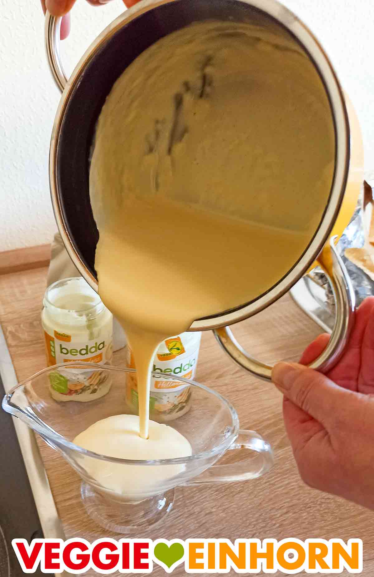 Zum Servieren wird die vegane Sauce Hollandaise von bedda in eine Sauciere gefüllt. Die vegane Sauce Hollandaise wird aus dem Kochtopf in eine Sauciere gegossen.