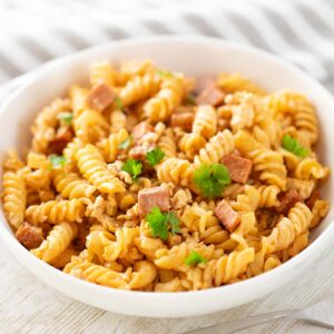 Nudeln mit veganem Leberkäse, serviert auf einem weißen Teller und mit Petersilie dekoriert.