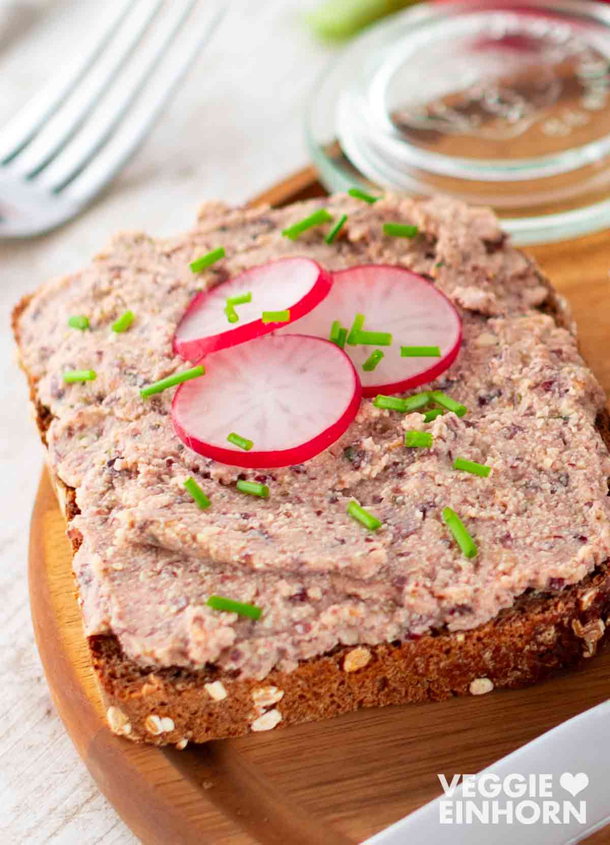 Eine Scheibe Vollkornbrot mit veganer Leberwurst, bestrichen mit der cremigen, leicht körnigen Streichwurst, garniert mit dünnen Radieschenscheiben und fein geschnittenem Schnittlauch.