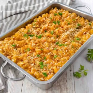 Vegane Mac and Cheese in einer rechteckigen Auflaufform mit cremiger Käsesoße, knusprigen Röstzwiebeln und Petersilie auf hellem Holztisch.