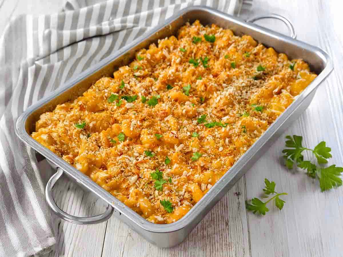 Vegane Mac and Cheese, goldbraun gebacken, mit Röstzwiebeln bestreut und in einer Metallform serviert.