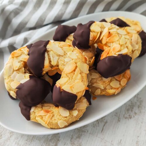 Vegane Mandelhörnchen auf einem Teller, überzogen mit Mandelblättchen und dunkler Schokolade.