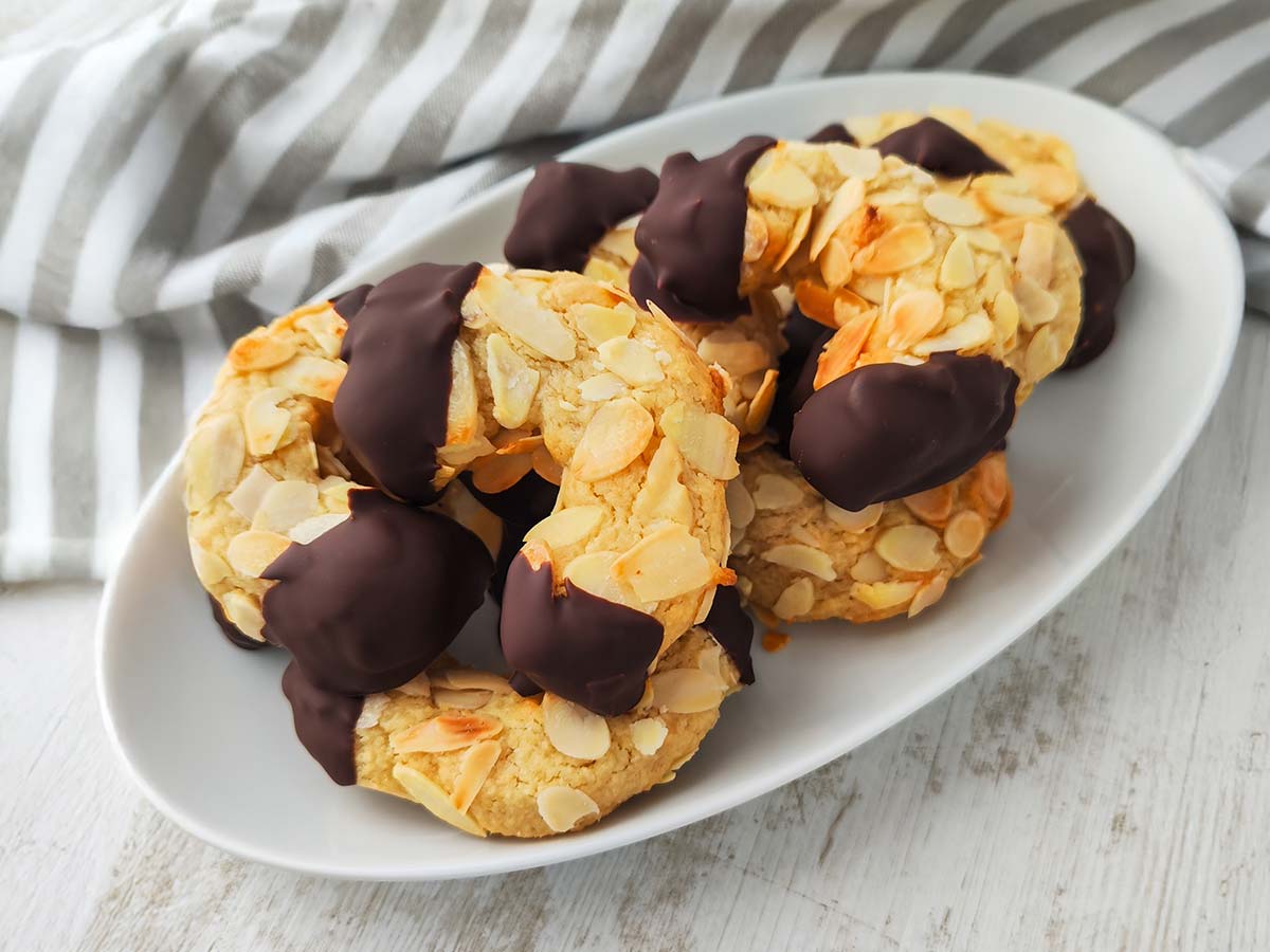 Vegane Mandelhörnchen auf einem Teller, überzogen mit Mandelblättchen und dunkler Schokolade.