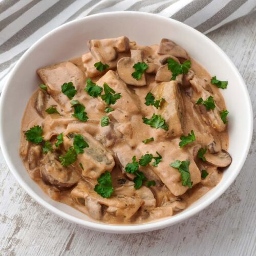 Vegane Maultaschen in Champignon Rahmsoße mit Petersilie auf einem weißen Teller.