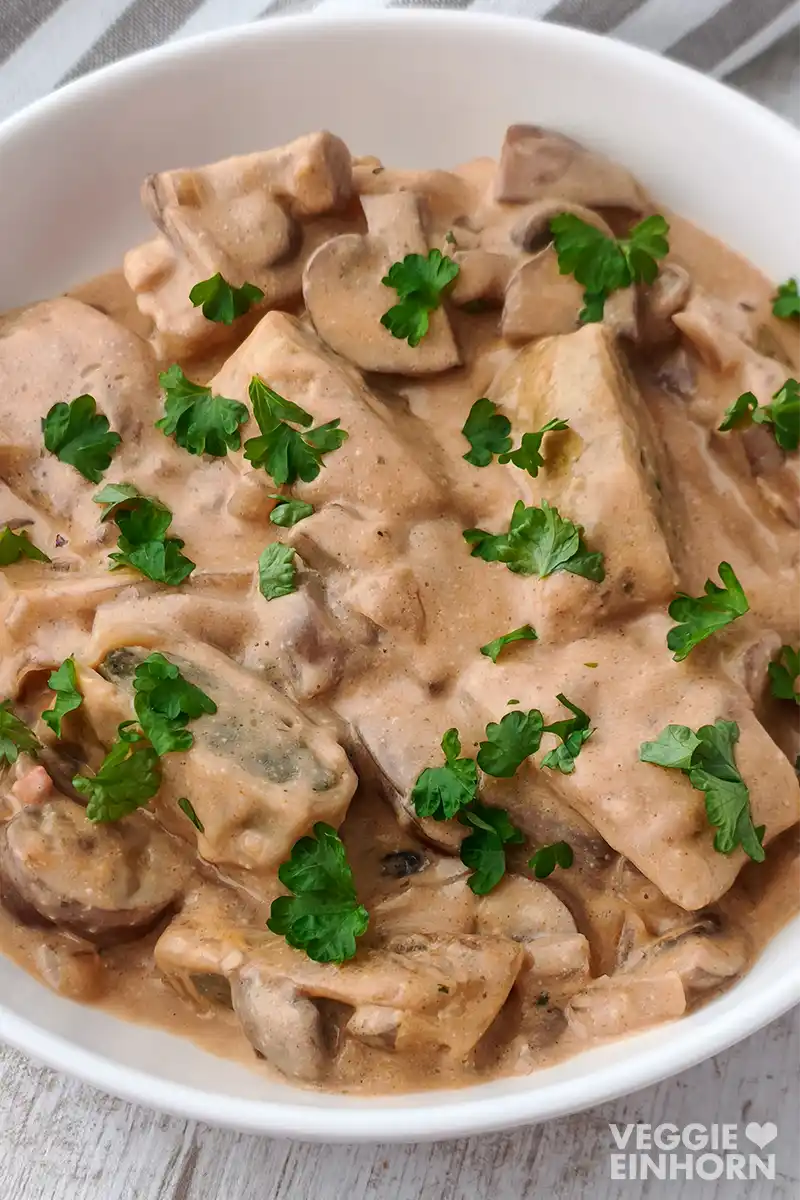 Nahaufnahme von veganen Maultaschen mit Champignons in Rahmsoße mit Petersilie bestreut.