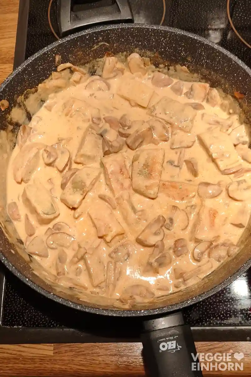 Pfanne mit veganen Maultaschen und Champignons in cremiger Rahmsoße auf einem Herd.