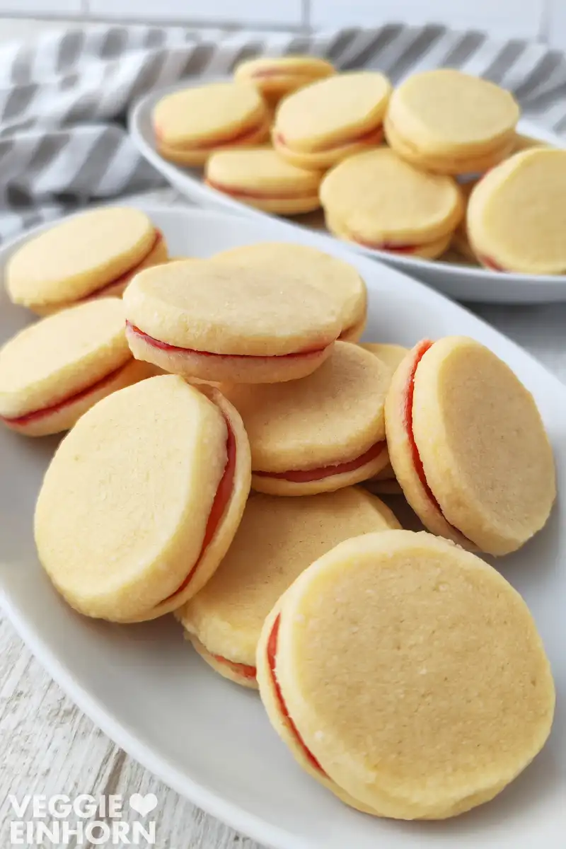 Zwei Teller mit veganen Marmeladenplätzchen stehen auf einem hellen Tisch.
