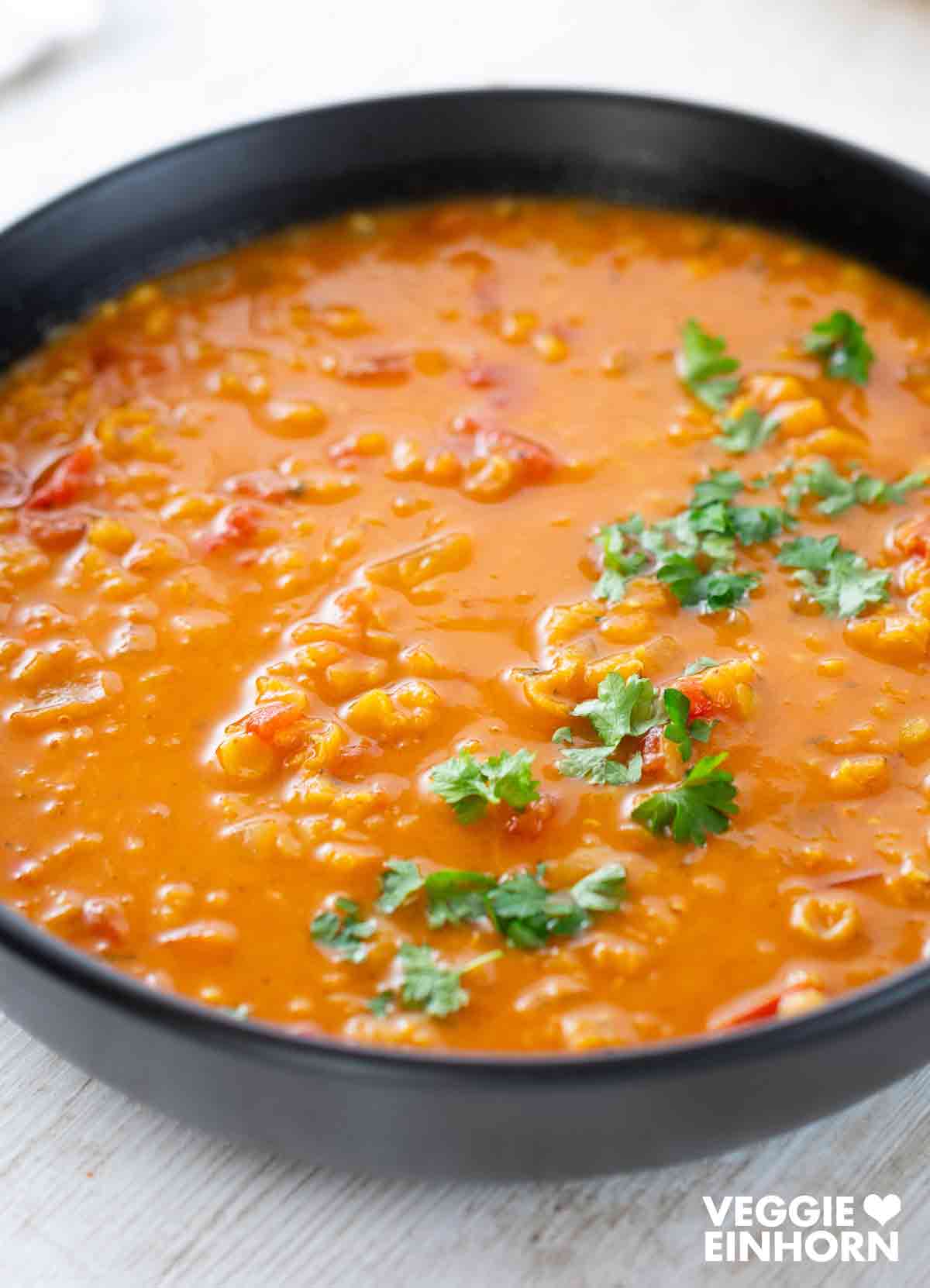 Eine cremige rote Linsensuppe mit Kokosmilch in einer schwarzen Schüssel, bestreut mit frischer Petersilie.