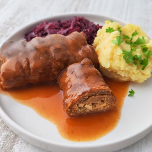 Vegane Roulade aus Soja Big Steaks mit Bratensoße auf einem Teller mit Kartoffelpüree und Rotkohl.