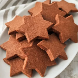 Vegane Schokoplätzchen in Sternform liegen auf einem weißen Plätzchenteller.