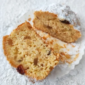 Halbierter veganer Stollen Muffin im Papierförmchen auf heller, mit Puderzucker bestäubter Fläche.