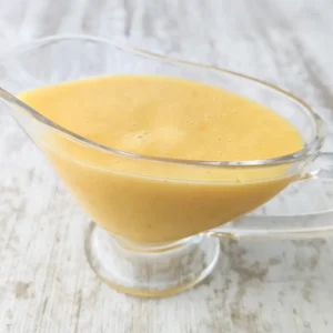 Vegane Vanillesoße in einer gläsernen Sauciere auf einem hellem Holztisch.