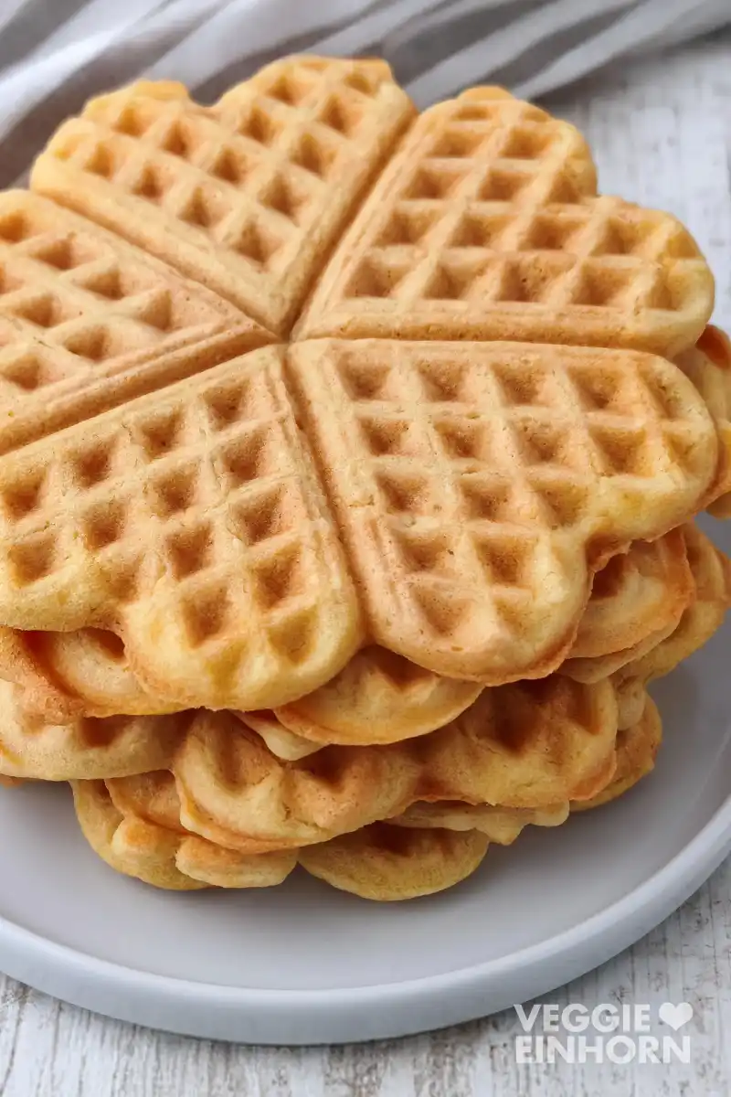 Nahaufnahme eines Stapels herzförmiger veganer Waffeln auf einem grauen Teller.
