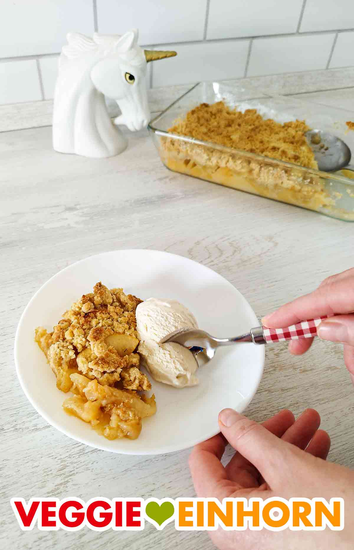 Apfel Crumble und vegane Vanilleeiscreme schmecken sehr gut zusammen. Apple Crumble und eine Kugel Vanilleeis mit einem Dessertlöffel