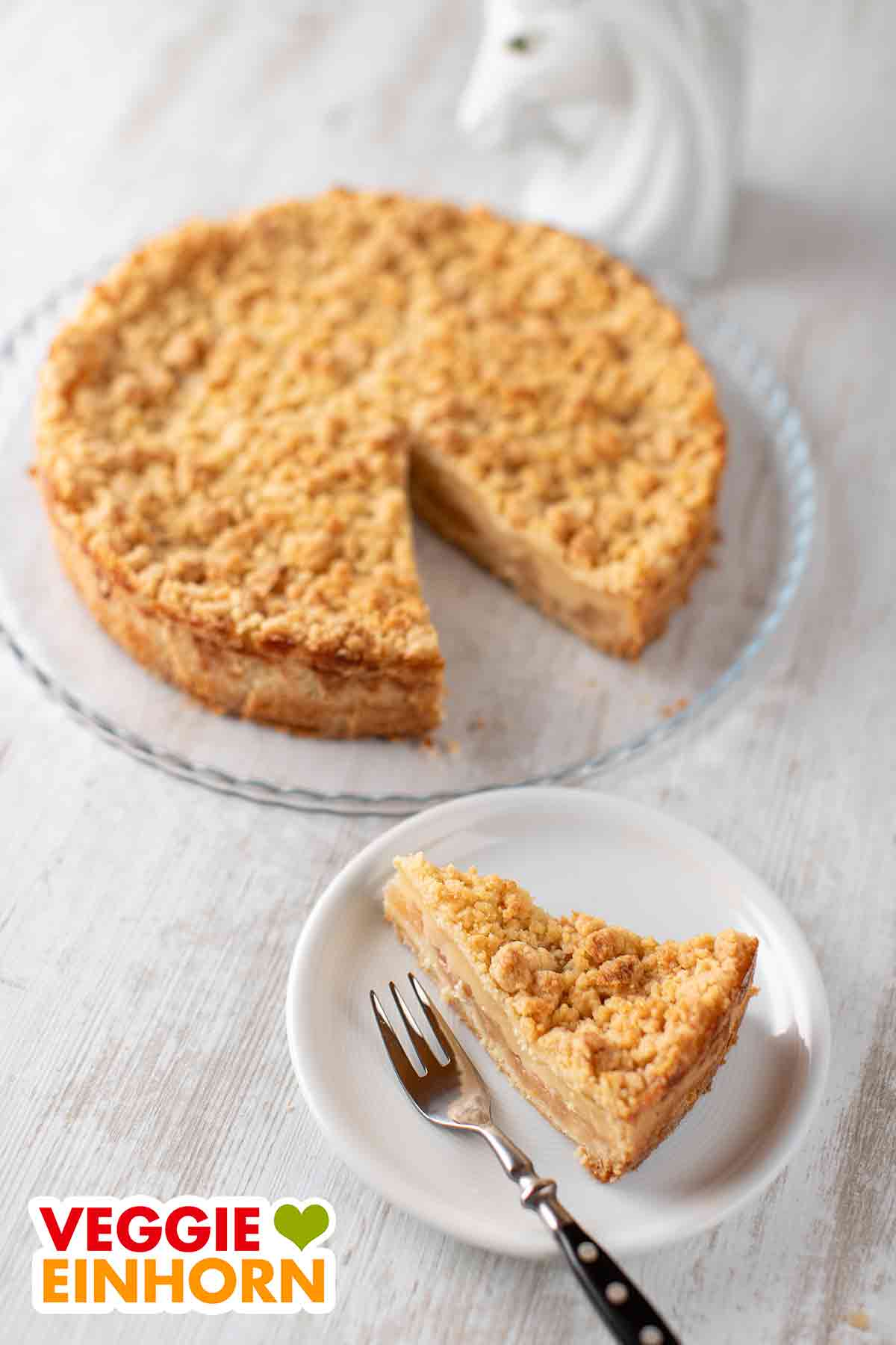 Der vegane Apfelkuchen mit Pudding und Streuseln ist saftig und lecker. Tortenplatte und Kuchenteller mit veganem Apfelkuchen mit Vanillepudding und Streuseln