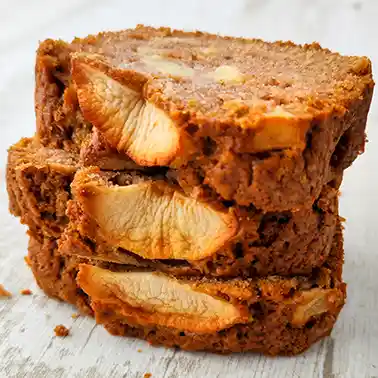 Drei übereinander gestapelte Stücke veganer Apfelkuchen aus der Kastenform, im Teig sind Apfelstücke sichtbar, der Kuchen liegt auf einem hellen Holztisch.