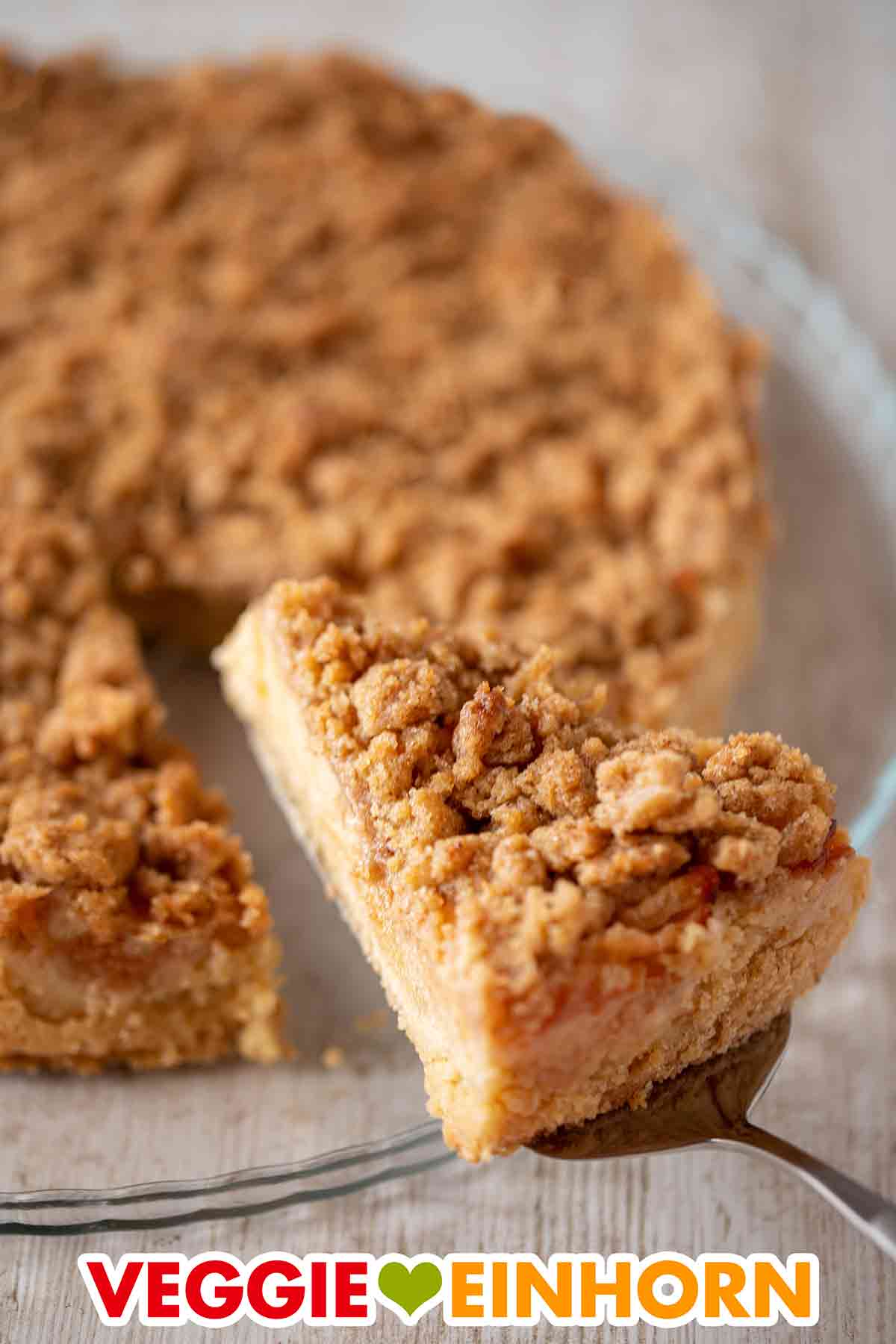Der vegane Apfelkuchen mit Mürbeteig und Zimtstreuseln wird serviert. Tortenheber mit einem Stück veganem Apfel Streuselkuchen