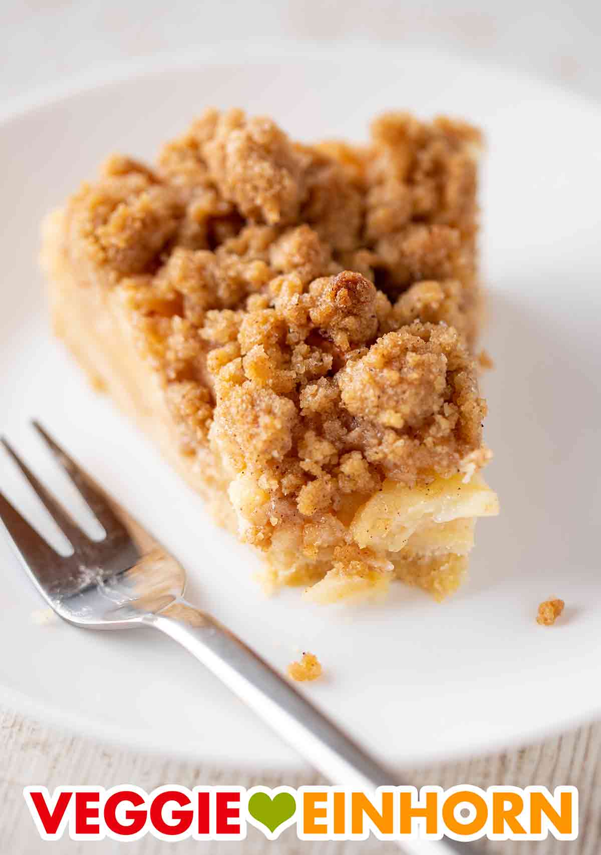 Der einfache vegane Apfel Streuselkuchen ist mit Mürbeteig. Veganer Apfelkuchen mit Zimtstreuseln auf einem Kuchenteller mit Kuchengabel