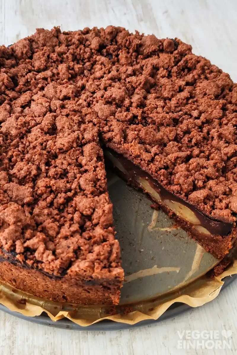 Nahaufnahme eines angeschnittenen veganen Birnenkuchens mit Schokostreuseln und Schokopudding.
