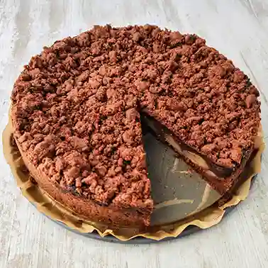 Ein runder veganer Schoko-Birnenkuchen mit Streuseln und Schokopudding, bei dem bereits ein Stück herausgeschnitten wurde.