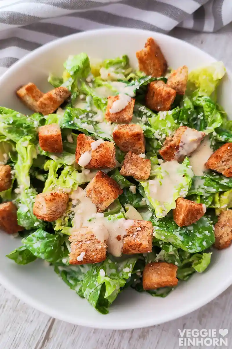Ein Teller mit Caesar Salat aus Römersalat und Croutons, die mit hellem cremigem Cashew-Dressing beträufelt sind.