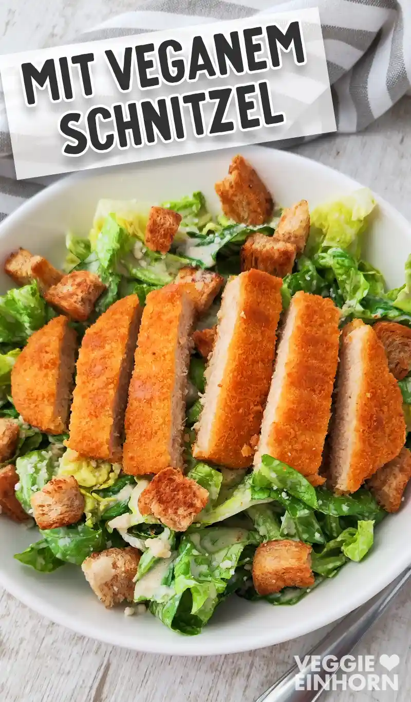Ein Teller mit veganem Caesar Salat und in Streifen geschnittenem veganem Schnitzel, das auf dem Salat liegt.