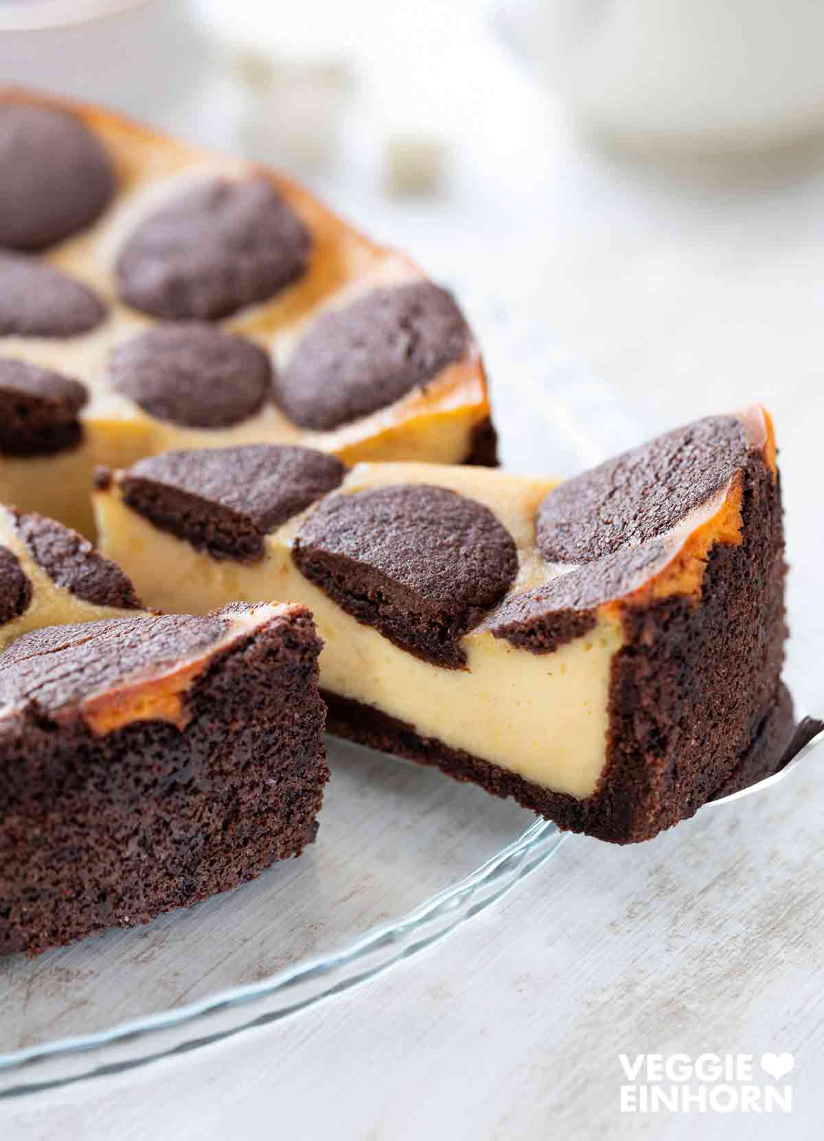 Ein angeschnittener veganer russischer Zupfkuchen mit cremiger Füllung und schokoladigem Mürbeteig auf einer Glasplatte.