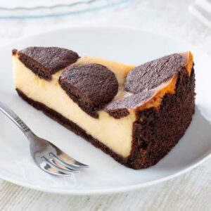 Ein Stück veganer russischer Zupfkuchen mit cremiger Füllung und schokoladigem Mürbeteigboden auf einem weißen Teller mit einer Kuchengabel.