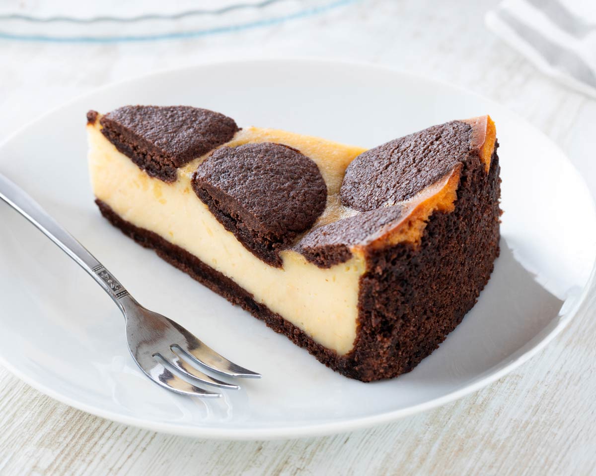 Ein Stück veganer russischer Zupfkuchen mit cremiger Füllung und schokoladigem Mürbeteigboden auf einem weißen Teller mit einer Kuchengabel.