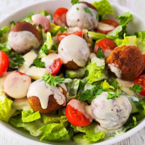 Falafel-Salat mit Romanasalat, Kirschtomaten, , Salatgurken und cremigem Dressing, serviert in einer weißen Schüssel.
