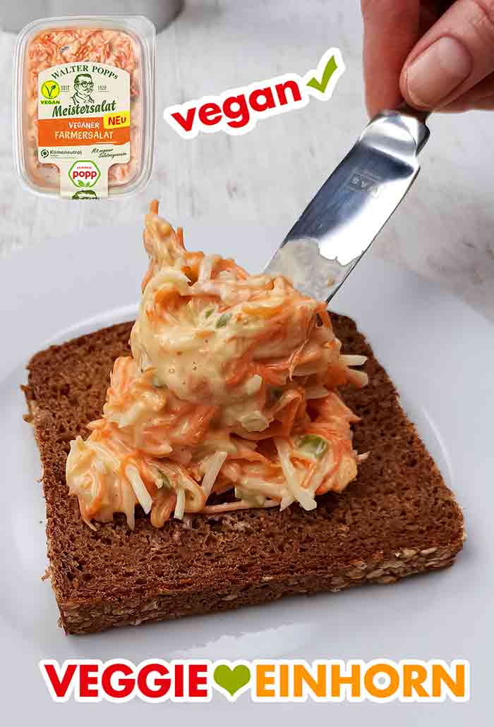 Der vegane Farmersalat von Popp schmeckt sehr gut. Veganer Farmersalat von Popp wird mit einem Messer auf einer Brotscheibe verteilt