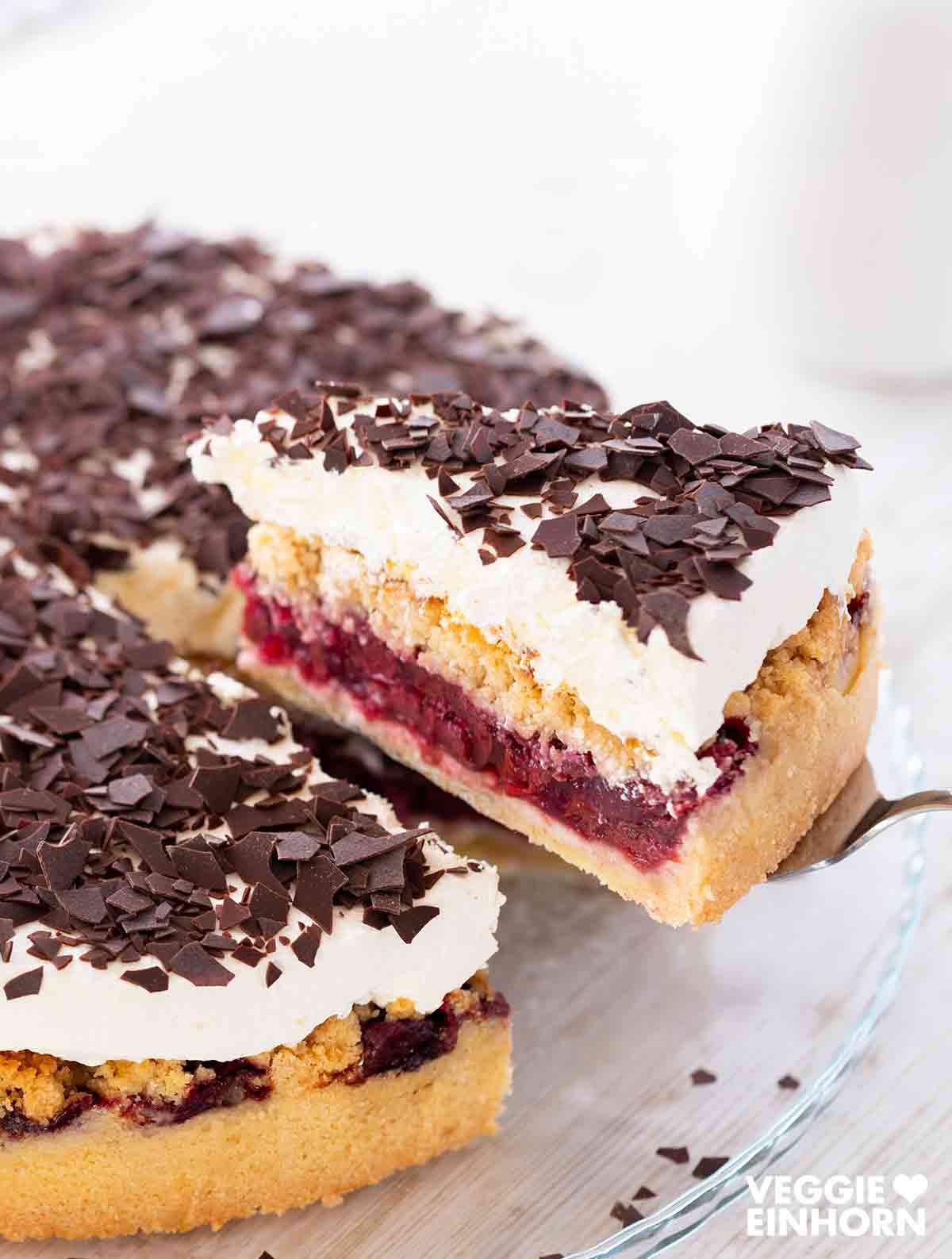 Ein Stück veganer Feuerwehrkuchen wird mit einem Tortenheber angehoben. Daneben steht der Kuchen auf einer Tortenplatte.