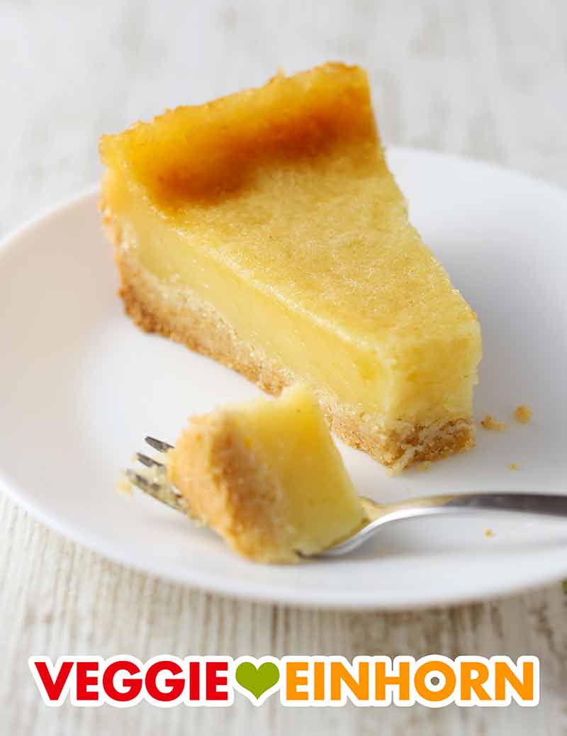 Der vegane Käsekuchen ohne Soja hat eine cremige Konsistenz durch den Kokosjoghurt. Ein Stück veganer Käsekuchen ohne Soja auf einem Kuchenteller mit einer Kuchengabel