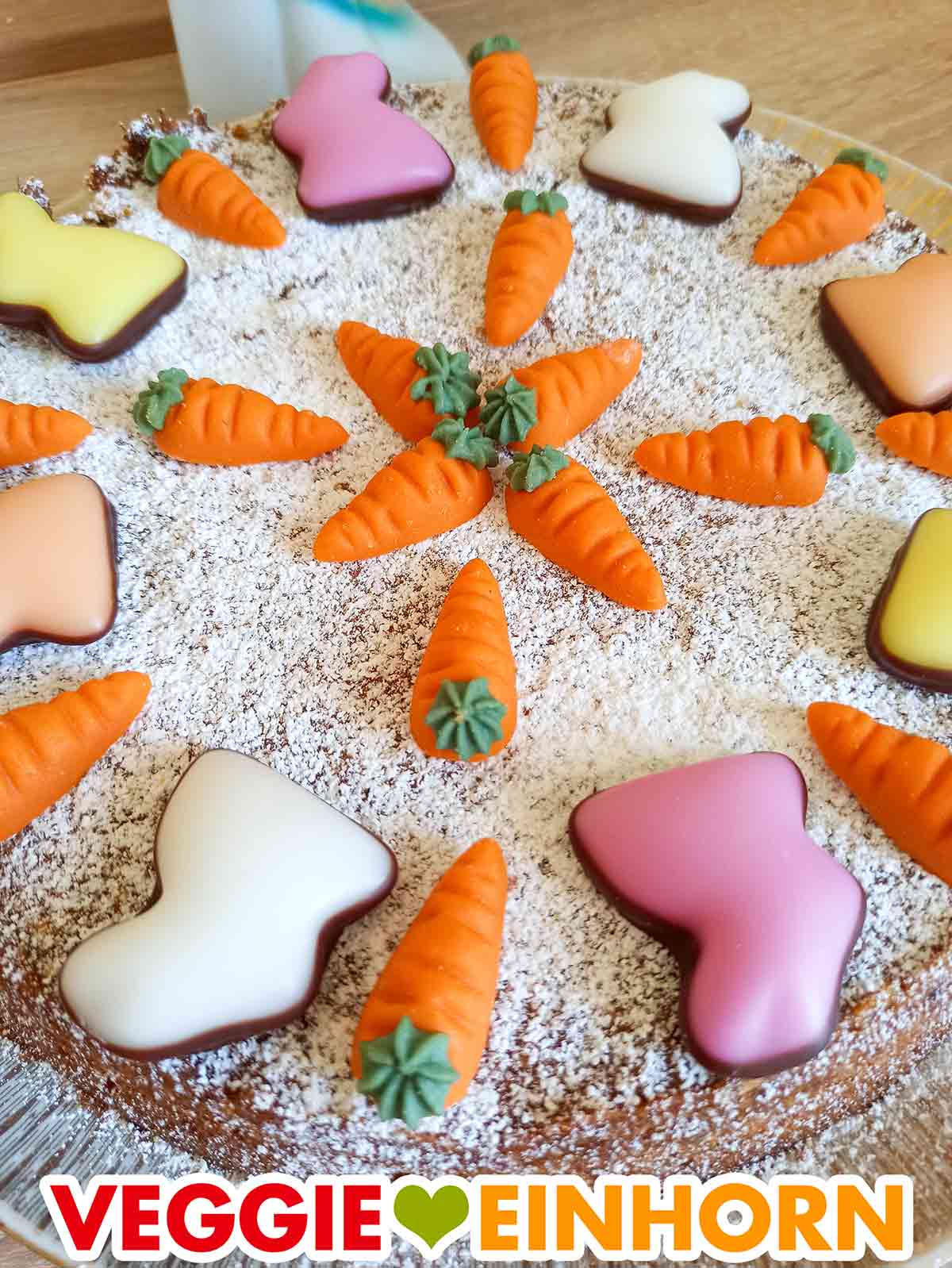 Fondant Hasen und Marzipankarotten auf einem veganen Karottenkuchen für Ostern Veganer Rüblikuchen dekoriert mit Puderzucker, Fondant Hasen und Marzipan Karotten