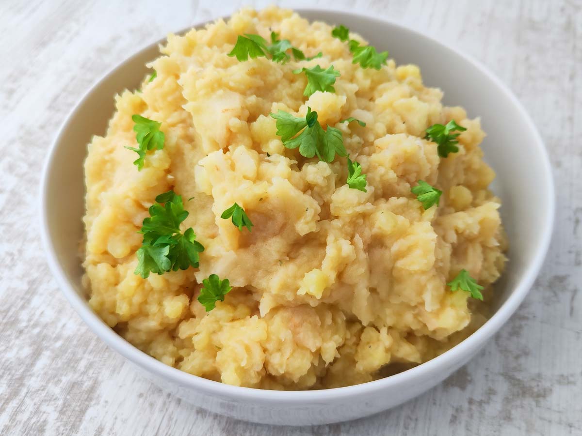 Kartoffel Sellerie Stampf mit Petersilie in einer weißen Schüssel auf hellem Holztisch.