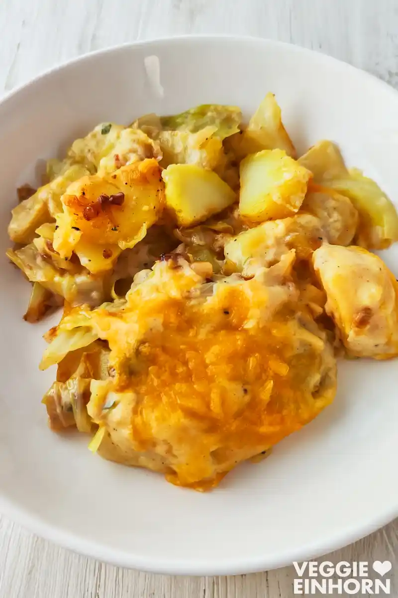 Nahaufnahme einer Portion veganen Kartoffel-Spitzkohl-Auflaufs mit geschmolzenem veganen Käse auf einem Teller.
