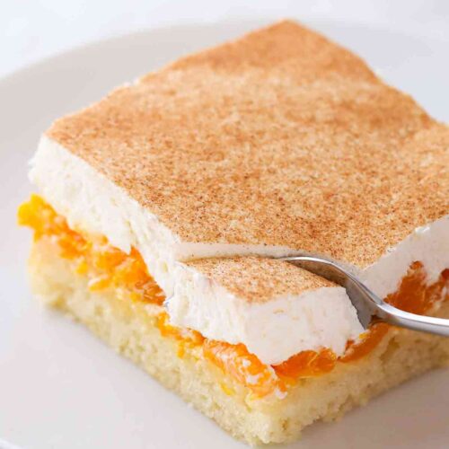 Ein Stück veganer Mandarinen-Schmand-Kuchen mit saftigen Mandarinen, veganer Sahneschicht und Zimt.