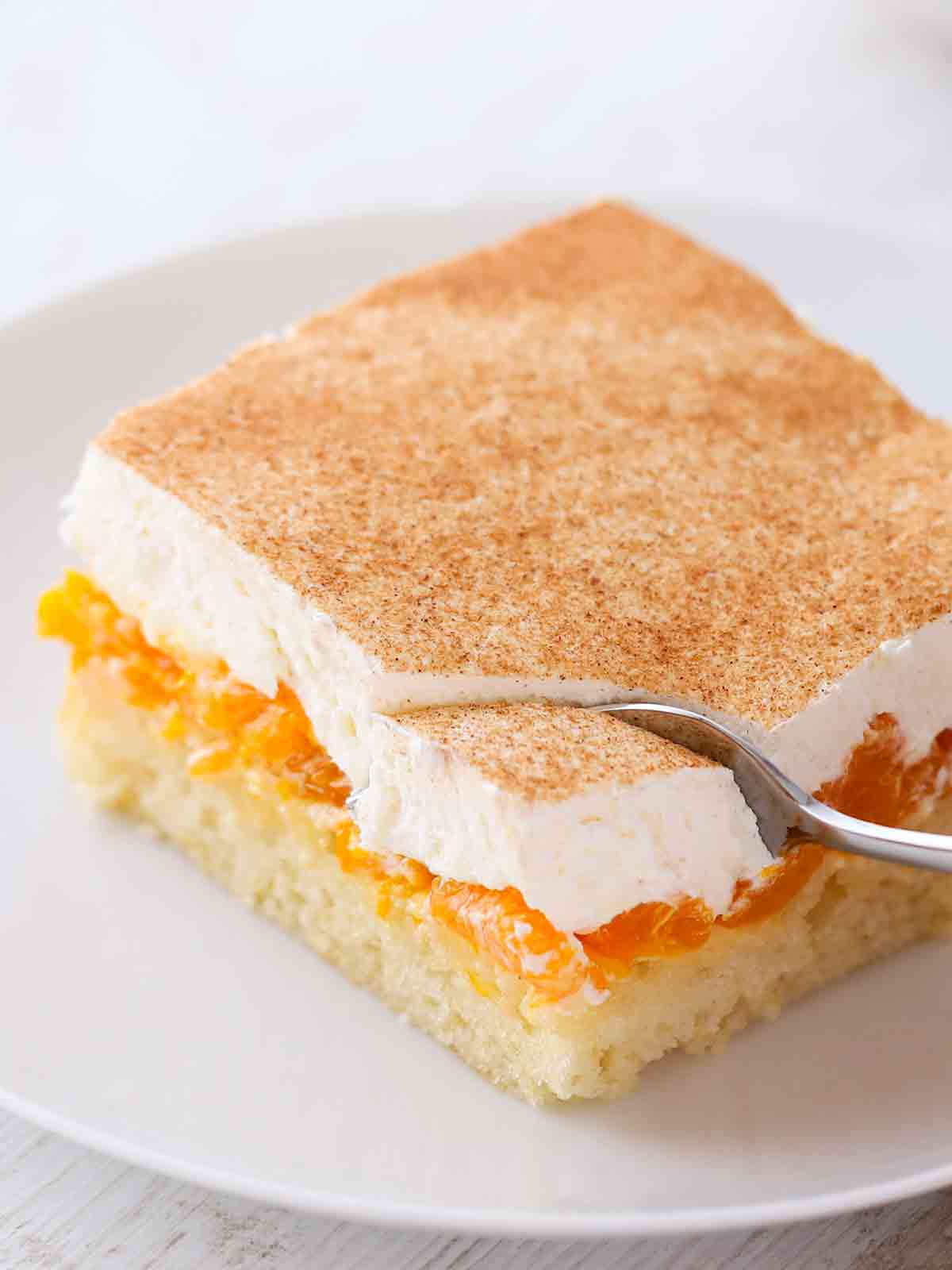 Ein Stück veganer Mandarinen-Schmand-Kuchen mit saftigen Mandarinen, veganer Sahneschicht und Zimt.