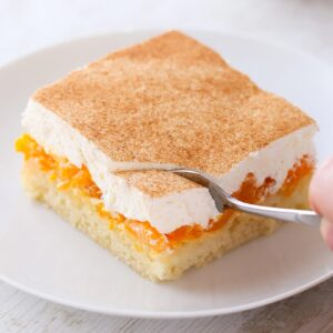 Ein Stück veganer Mandarinen-Schmand-Kuchen auf einem weißen Teller wird mit einer Gabel geteilt.