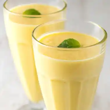 Zwei Gläser mit veganem Mango Lassi, dekoriert mit frischer Minze.