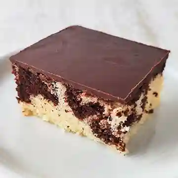 Ein saftiges Stück veganer Marmorblechkuchen mit Schokoladenglasur auf einem weißen Teller.