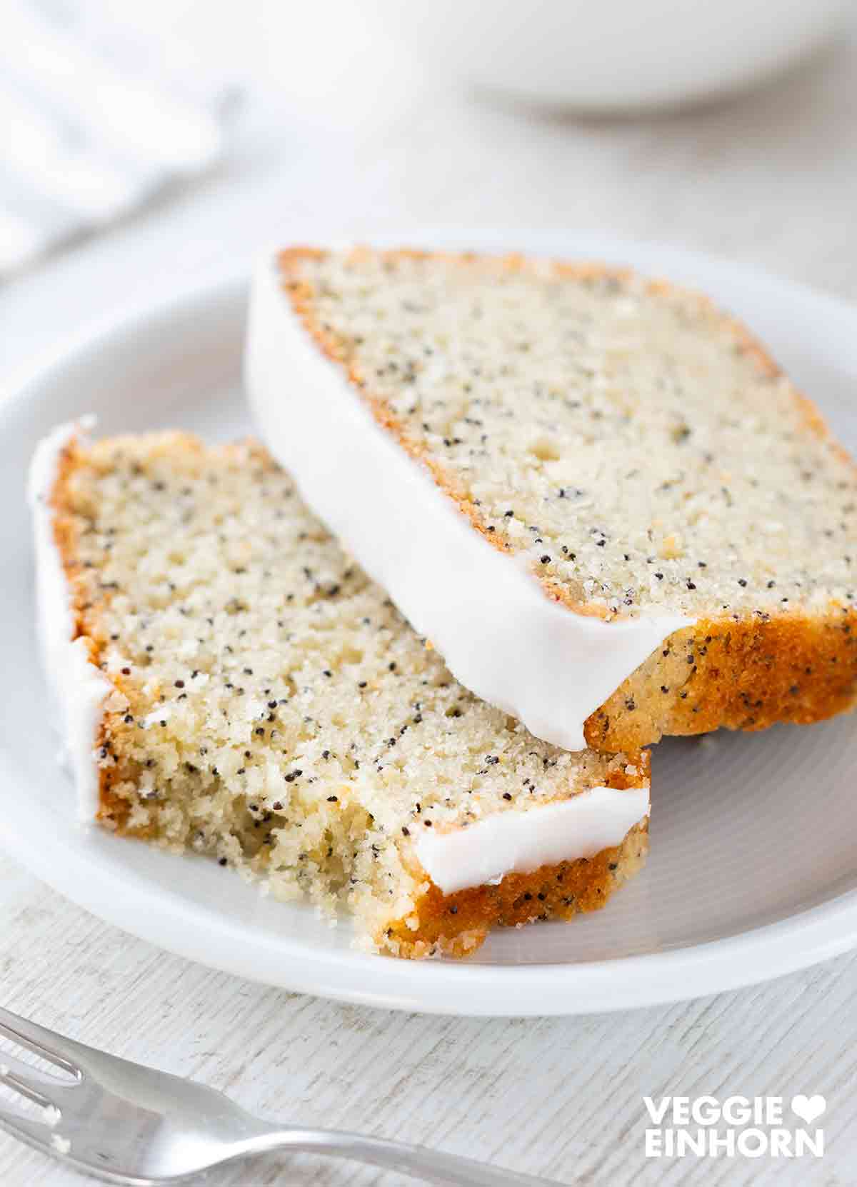 Zwei Stücke veganer Zitronenkuchen mit Mohn auf einem Teller.