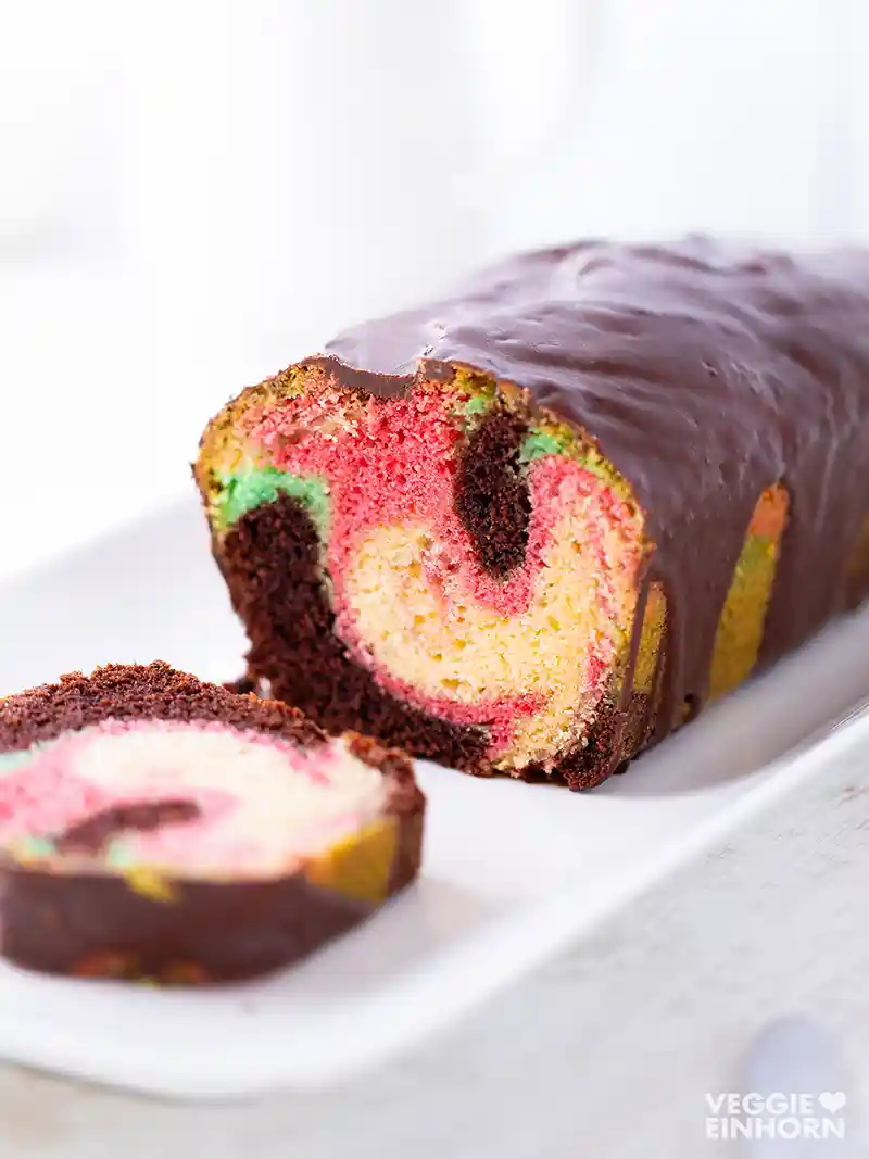 Angeschnittener veganer Papageienkuchen mit buntem Teig und Schokoglasur.
