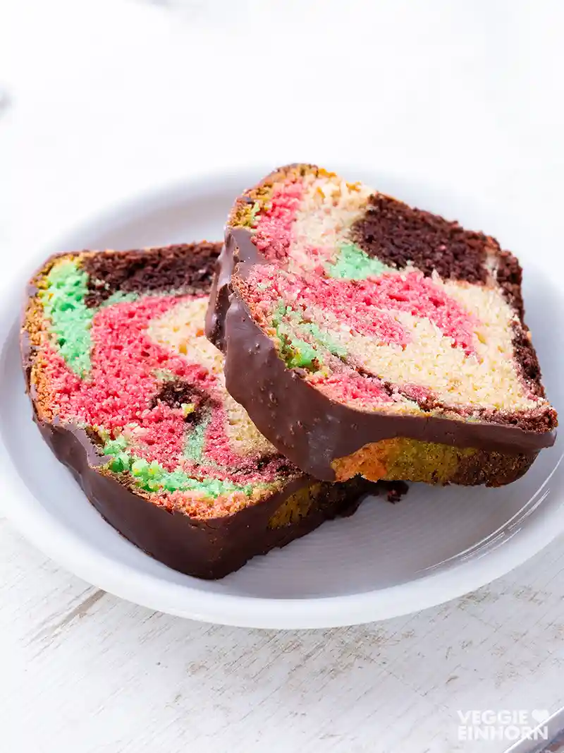 Zwei Stücke bunt marmorierter veganer Papageienkuchen auf einem Teller.